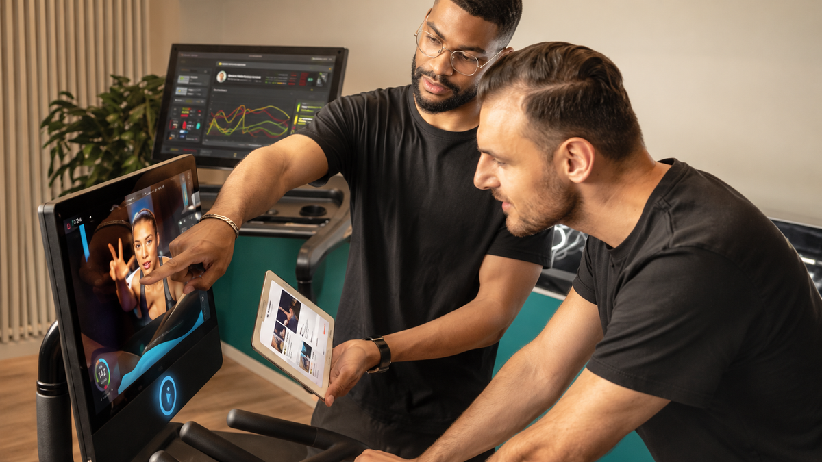 Zwei Kollegen besprechen Trainingsdaten an Laufband-Display und Tablet während der Produktentwicklung