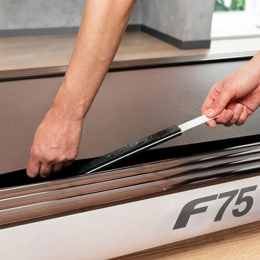 Zwei Hände schieben den geölten Applikatorstab unter das angehobene Laufband eines Sportstech F75