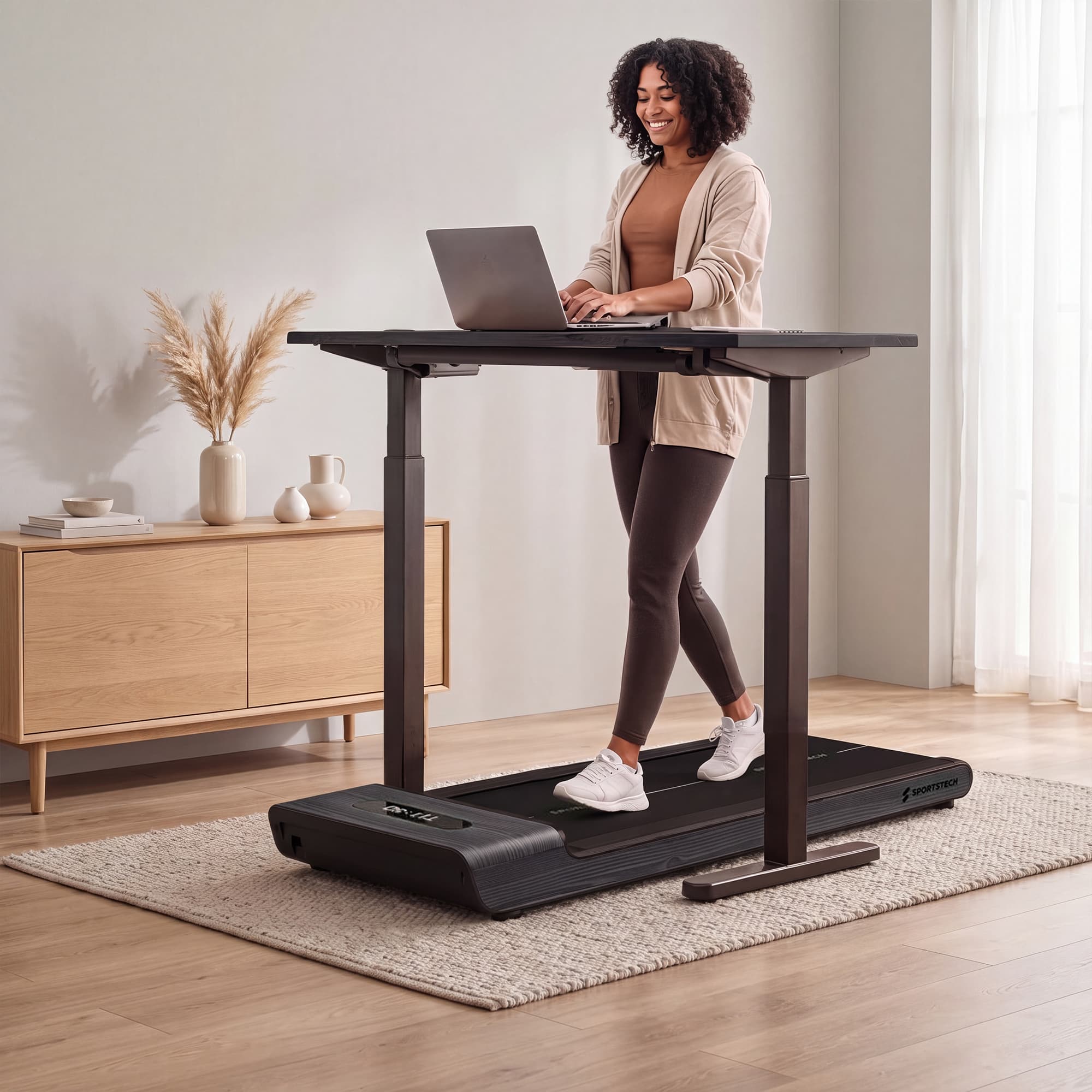 Frau geht auf grauem WoodPad Pro unter höhenverstellbarem Stehschreibtisch mit Laptop