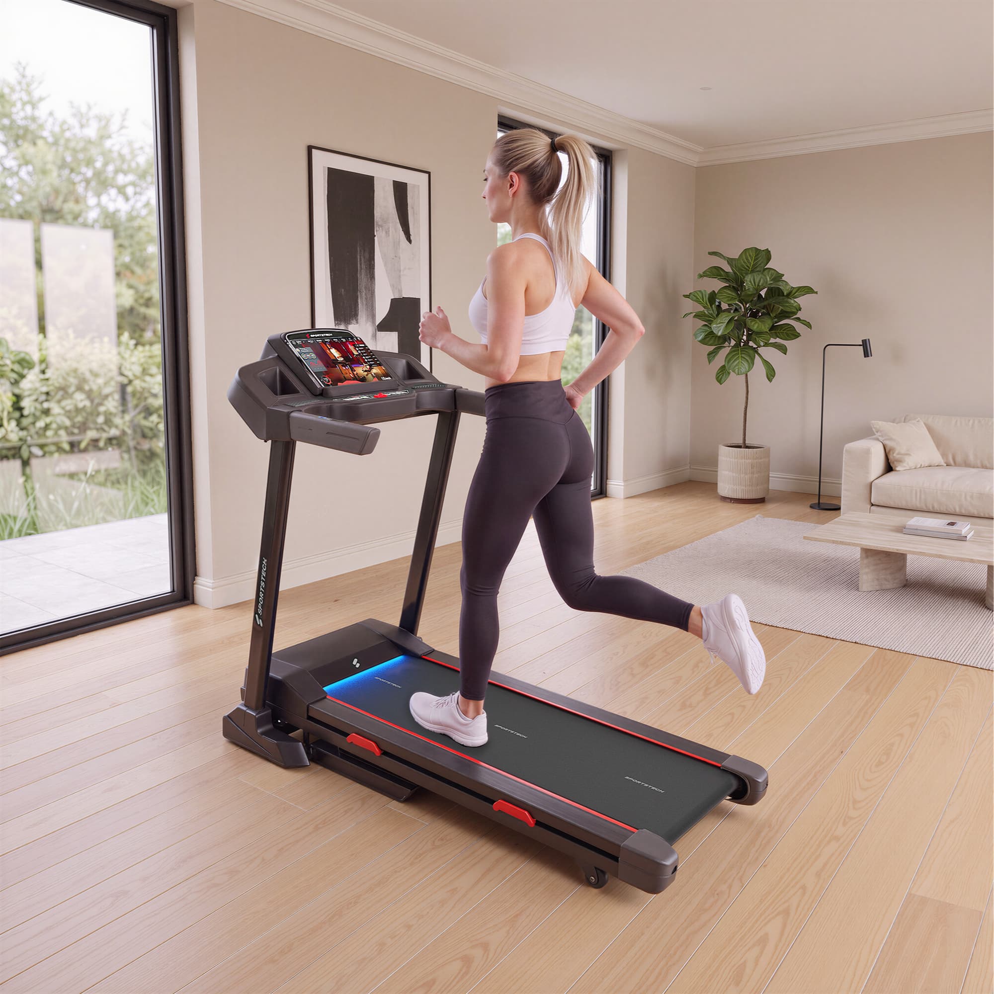 Frau joggt auf dem F31s Laufband in einem hellen Wohnzimmer mit Fenster und Sofa