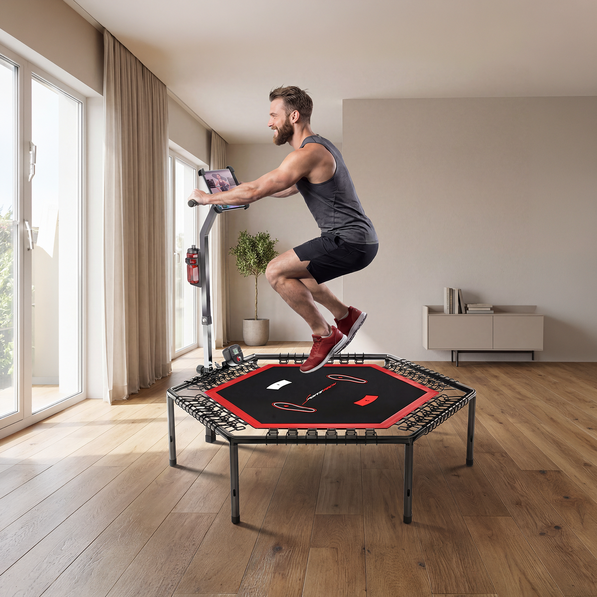 Mann trainiert auf dem HTX100 Trampolin in einem hellen Wohnraum mit Holzboden und großen Fenstern