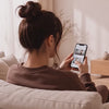 Frau startet die Sportstech Live App am Smartphone und geht auf dem sWalk Lite vor einer Outdoor-Strecke am Fernseher