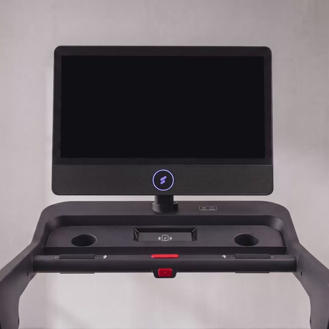 Frau trainiert im Ausfallschritt neben dem sTread Pro, auf dem Touchdisplay laeuft ein gefuehrtes Workout