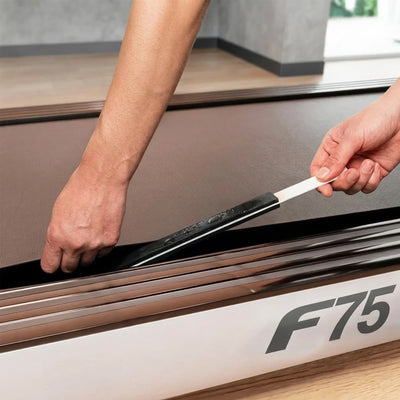 Zwei Hände schieben den geölten Applikatorstab unter das angehobene Laufband eines Sportstech F75