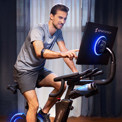 Mann mit sPulse Sensor am Handgelenk auf Sportstech Indoor-Bike, tippt auf blau leuchtenden Touchscreen
