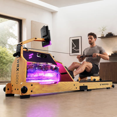 Mann rudert im Wohnzimmer am hellbraunen WRX1000, pink leuchtender Wassertank mit WRX1000-Schriftzug