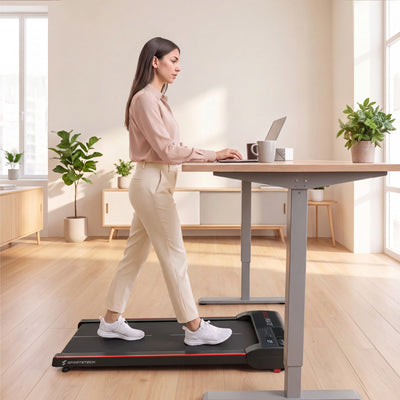 Frau geht auf dem Walkmate Walking Pad unter einem Stehschreibtisch mit Laptop
