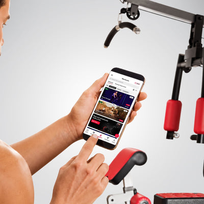 Mann bedient die Trainings-App auf dem Smartphone neben der HGX200 Kraftstation