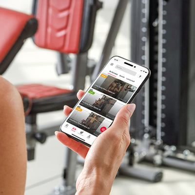 Hand hält Smartphone mit Trainings-App vor der HGX300 Kraftstation