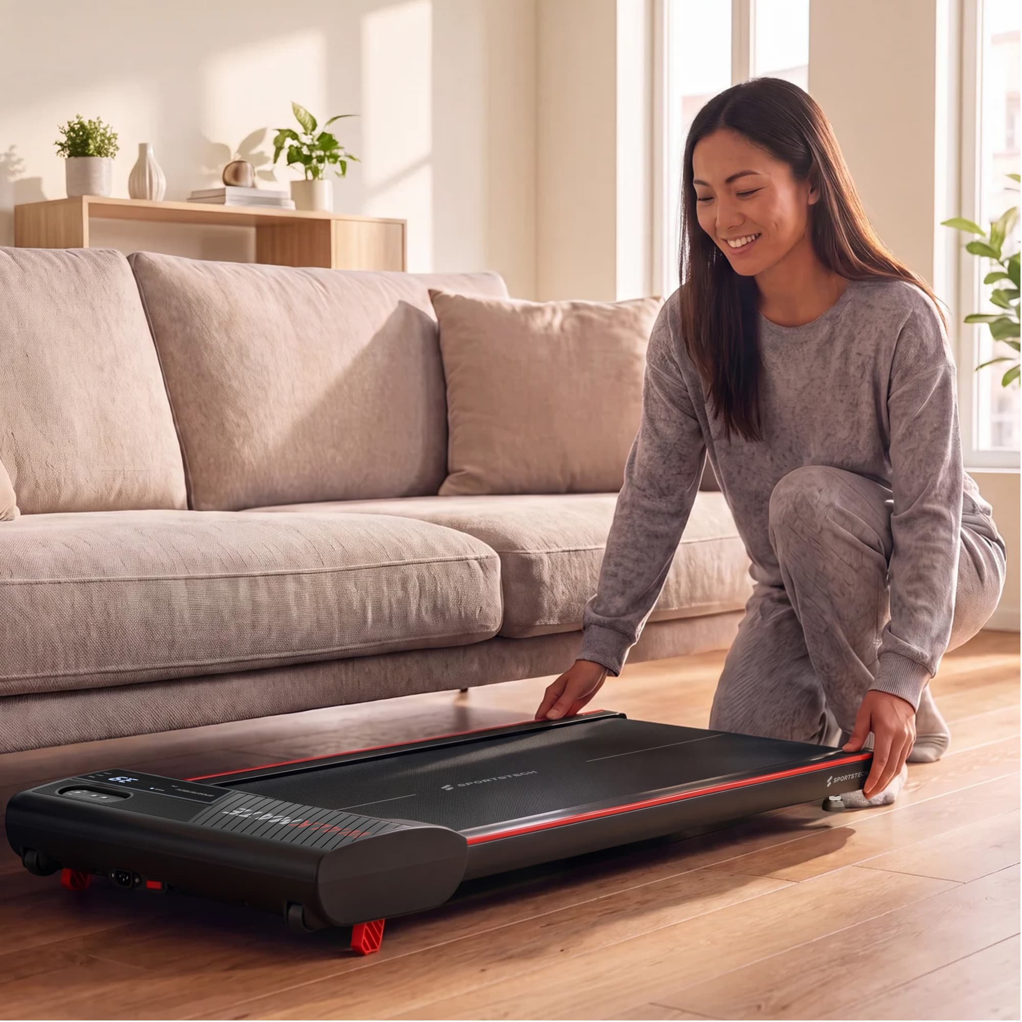Frau schiebt das flache Walkmate Walking Pad unter ein Sofa im Wohnzimmer