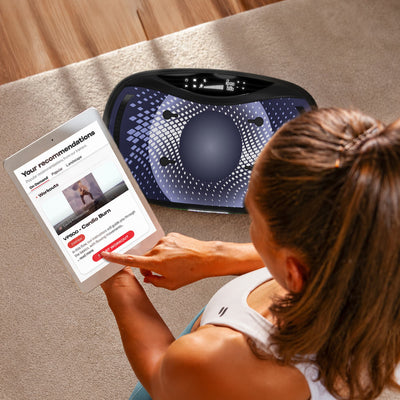 Frau steuert Workout-App auf Tablet neben der VP500 Vibrationsplatte am Boden