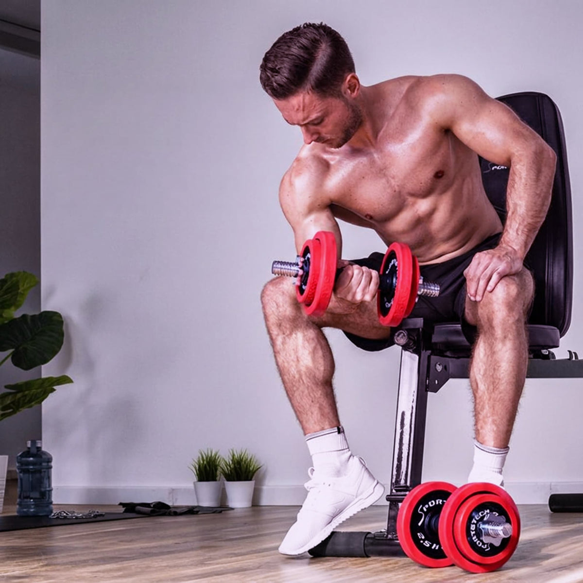 Mann trainiert sitzend auf einer Trainingsbank Bizeps-Curls mit einer rot bestückten AH300 Kurzhantel