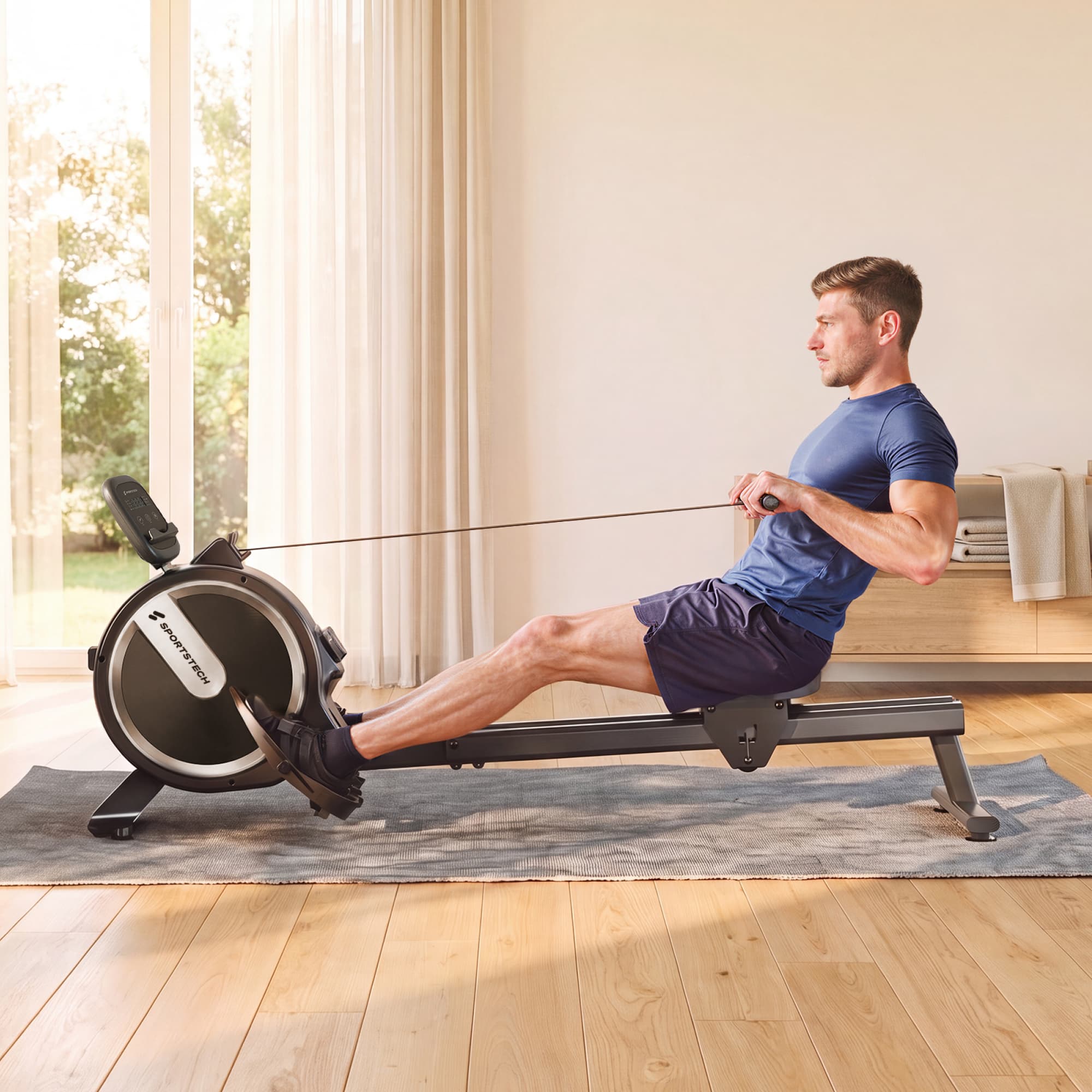 Mann rudert auf dem Sportstech PROwer Lite Rudergerät im Wohnzimmer