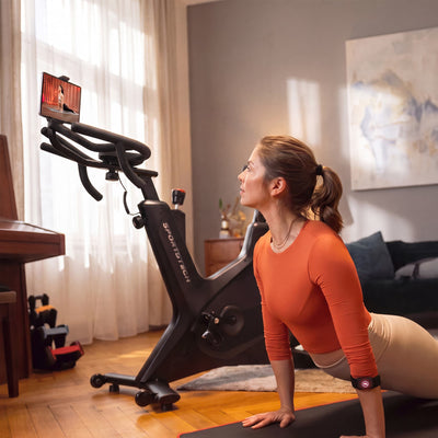 Frau dehnt sich auf der Matte vor dem sBike Lite, auf dem Tablet an der Halterung läuft ein Kursvideo
