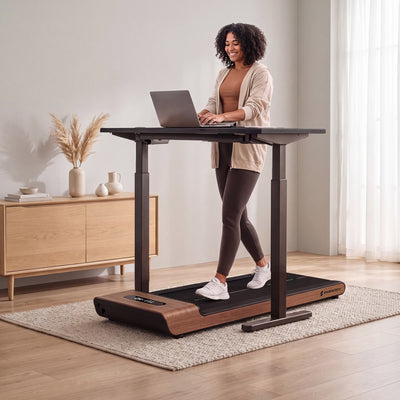 Frau geht auf dunkelbraunem WoodPad Pro unter höhenverstellbarem Stehschreibtisch mit Laptop