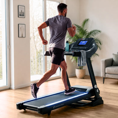 Mann joggt auf dem F37s Laufband in einem hellen Wohnzimmer, Ansicht von hinten