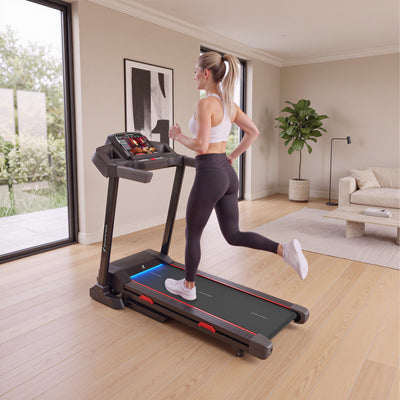 Frau joggt auf dem F31s Laufband in einem hellen Wohnzimmer mit Fenster und Sofa