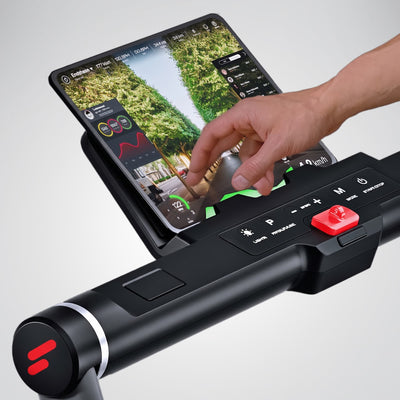Hand bedient die Touch-Konsole des sWalk Plus mit roter Stopptaste, daneben Tablet mit Lauftraining