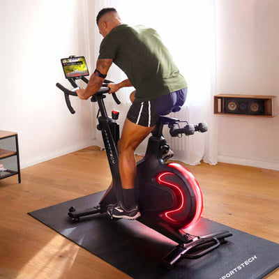 Sportler tritt im Wohnzimmer auf dem sBike Lite in die Pedale, das Schwungrad leuchtet dabei rot