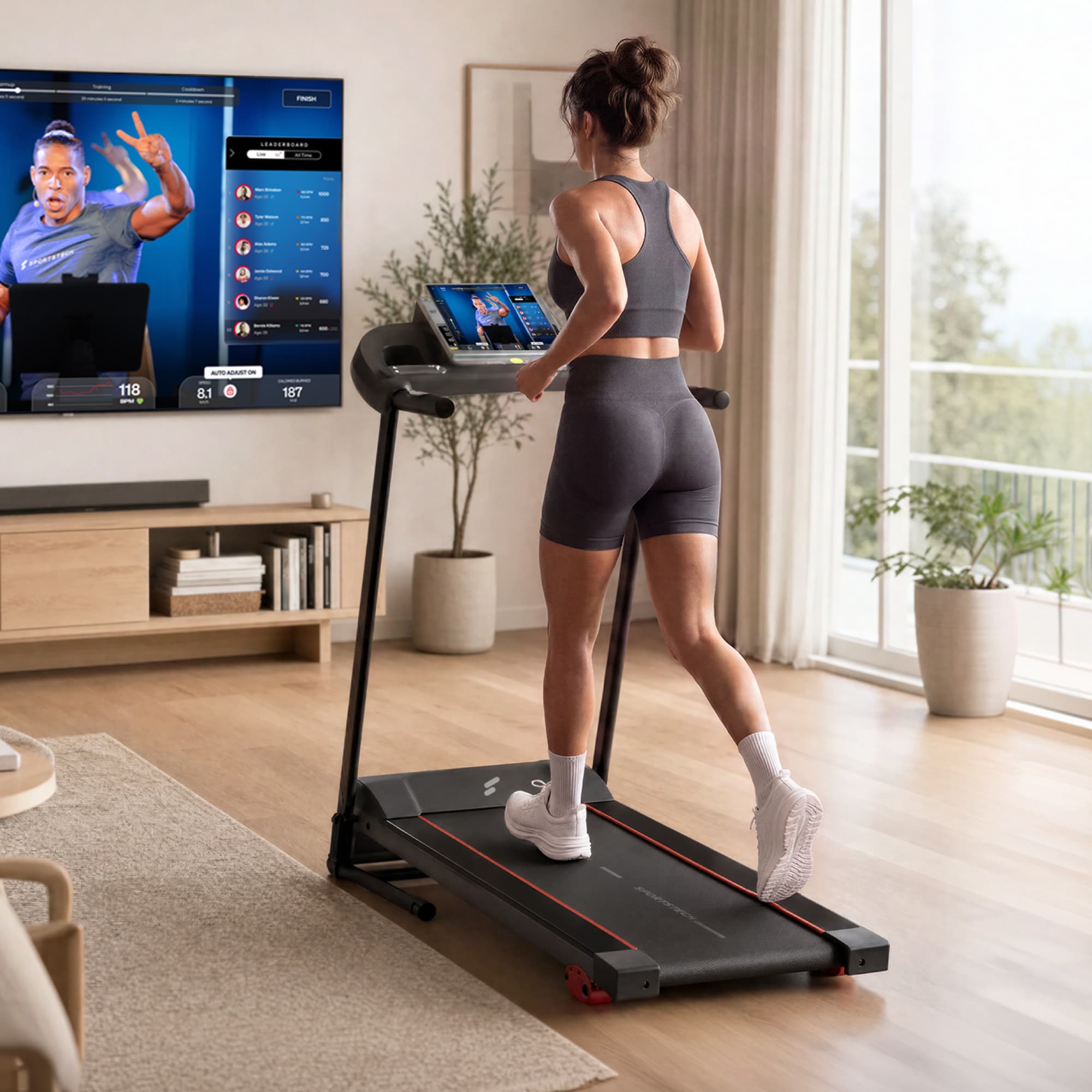 Frau läuft von hinten gesehen auf dem F10 Laufband, an der Wand ein Bildschirm mit Trainingsapp