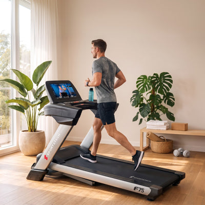 Mann läuft im hellen Wohnraum am F75 Profi-Laufband, Zimmerpflanzen und Hanteln im Hintergrund