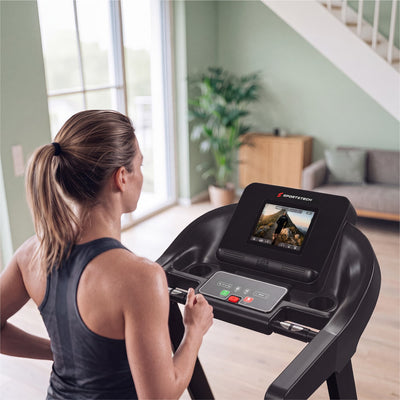 Nahaufnahme der F37s Pro Konsole mit Touchdisplay und Bedientasten, Frau hält den Griff, Wohnraum im Hintergrund