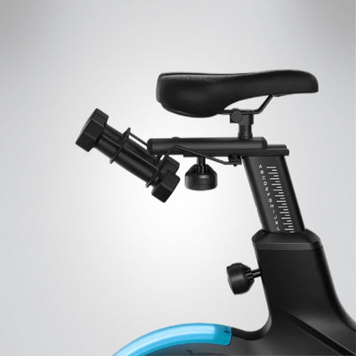 Detail von Sattel, Sattelstütze mit Skala und Hantelhalter am sBike Lite über türkis leuchtendem Schwungrad