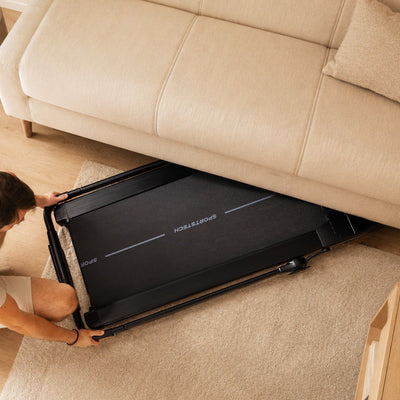 Person schiebt das zusammengeklappte flache sPad1000 Laufband unter ein Sofa