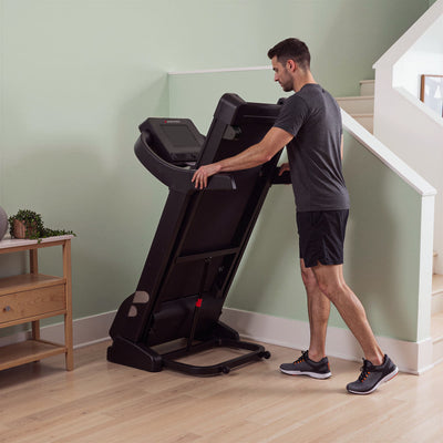 Mann klappt das F37s Pro Laufband platzsparend hoch, senkrecht stehendes Deck an einer grünen Wand