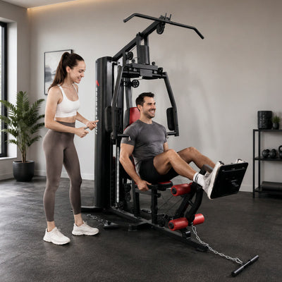Frau assistiert einem sitzenden Mann bei der Beinstreckung an der HGX150 Kraftstation im Trainingsraum