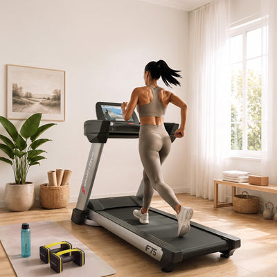 Frau läuft von hinten gesehen am F75 Profi-Laufband, helles Zimmer mit Pflanze und Trainingszubehör