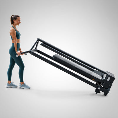 Frau zieht die zusammengeklappte sGym Pro an der Stange auf Transportrollen