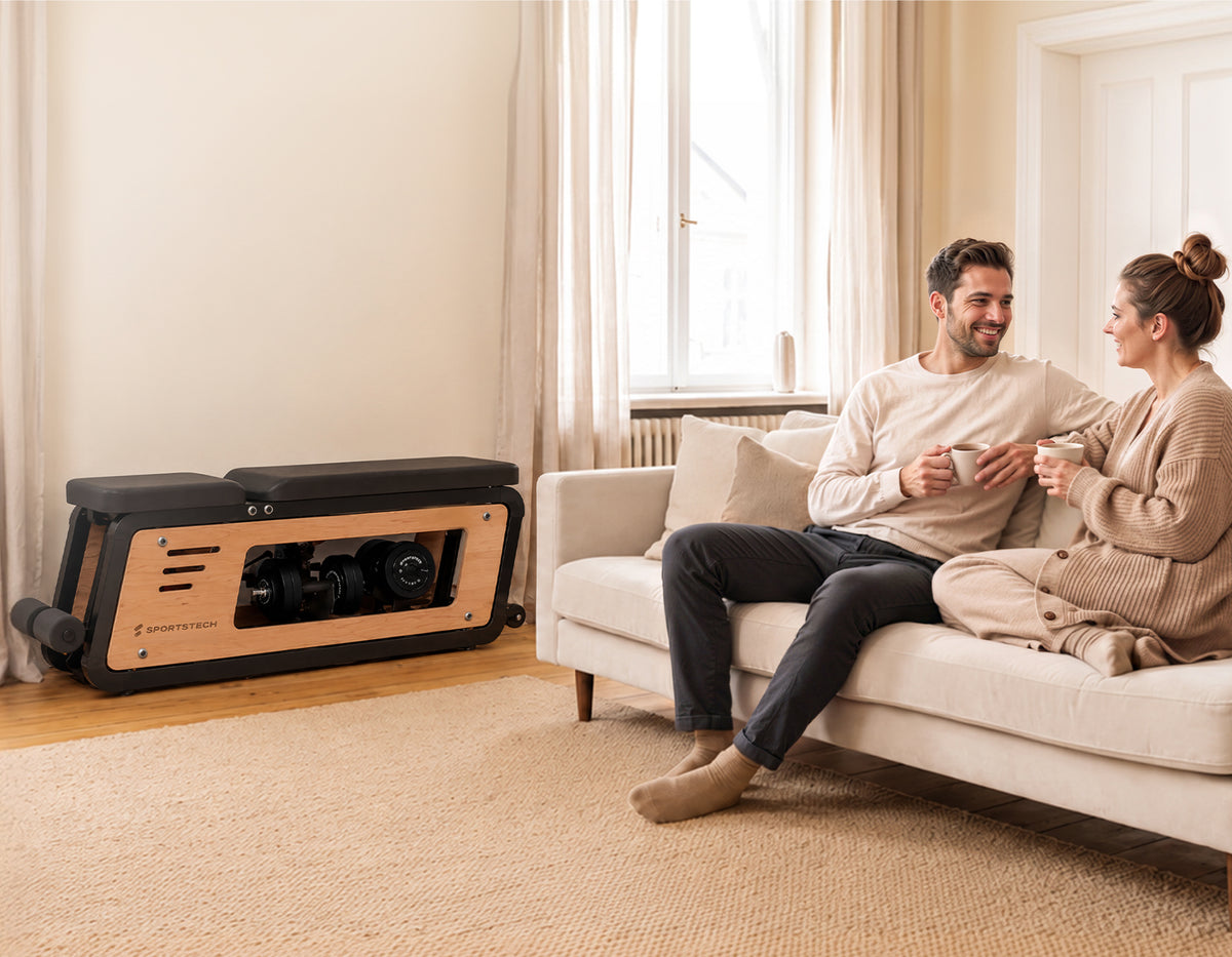 Sportstech Woodmate Lite Hantelbank im Wohnzimmer, Paar entspannt auf dem Sofa daneben