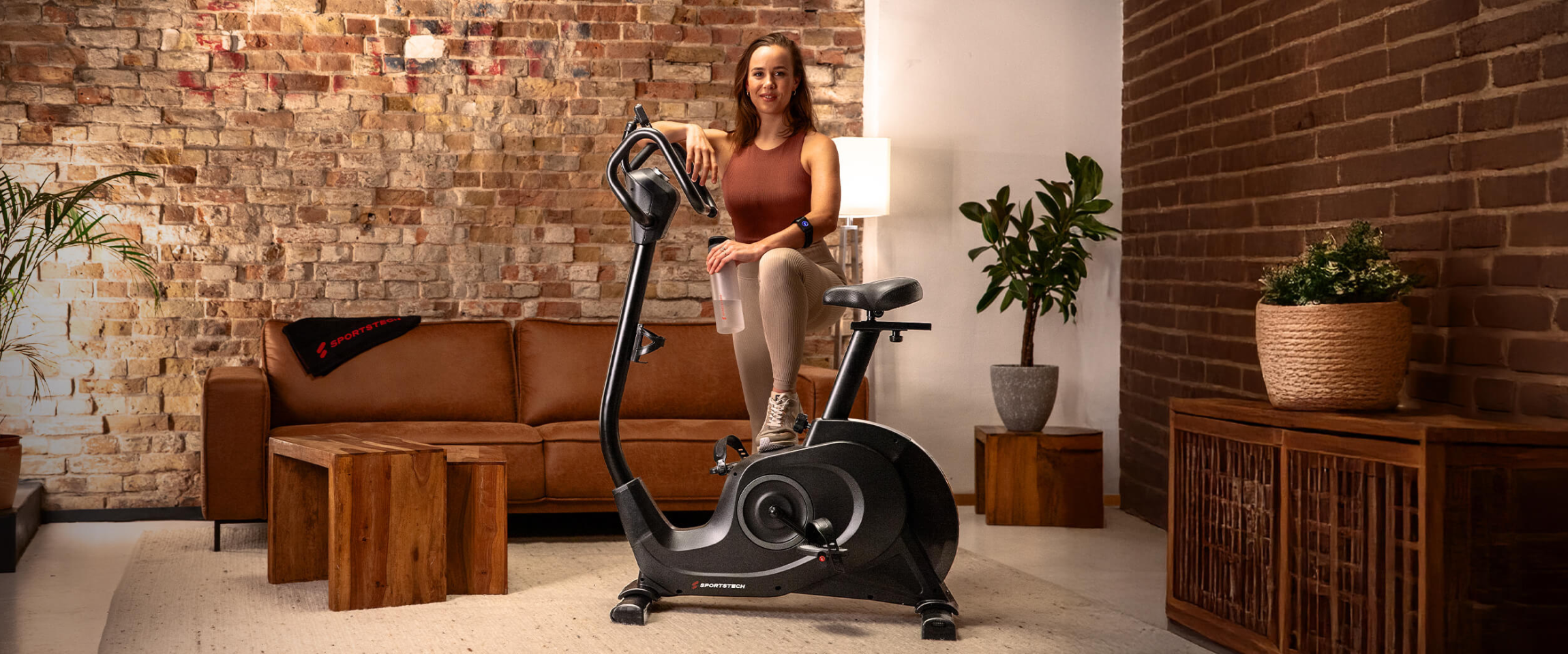 Eine Frau steht vor einem Ergometer in ihrem Wohnzimmer